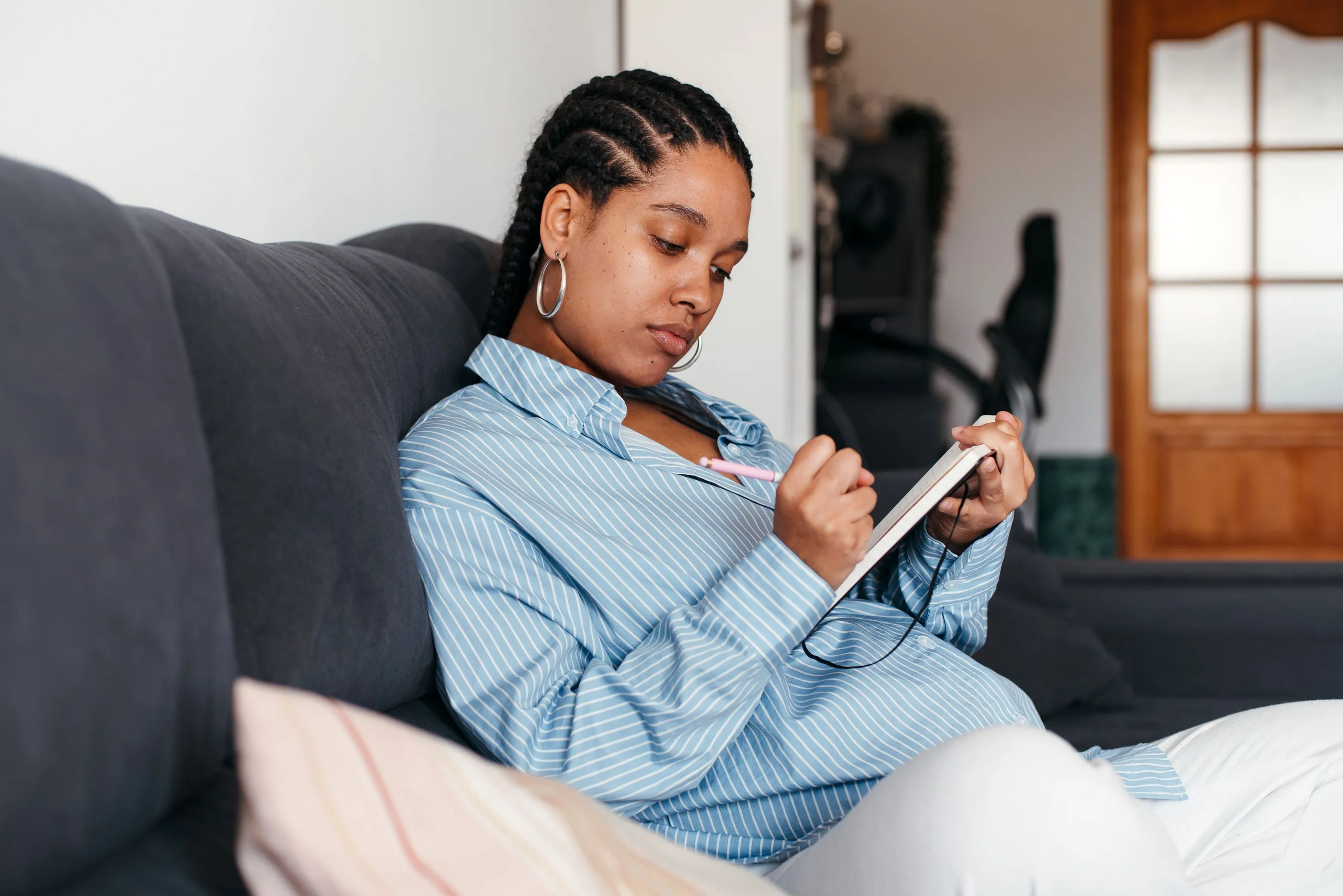 pregnant woman sitting on couch writing